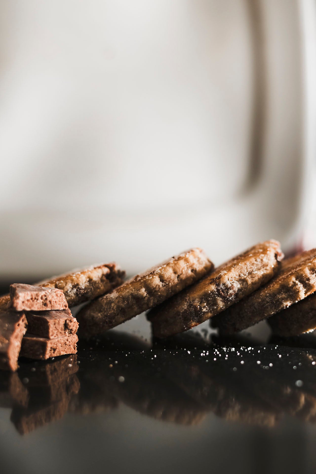 Close up of Dragonstone Bakes chocolate chip welsh cakes lying down next to a chunk of dairy milk chocolate on a dark reflective surface.