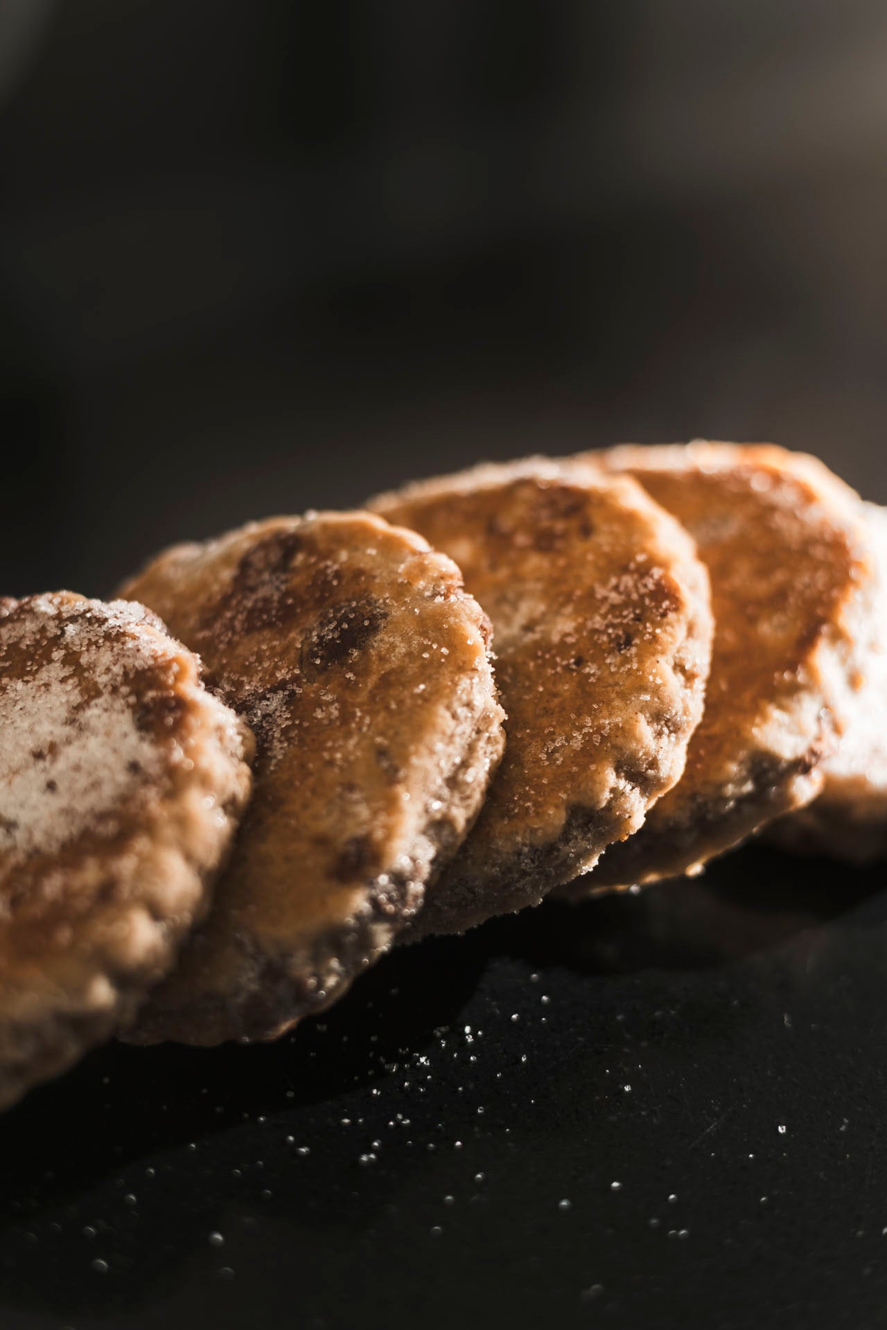 A row of Dragonstone Bakes chocolate chip Welsh Cakes lying down on a black surface.