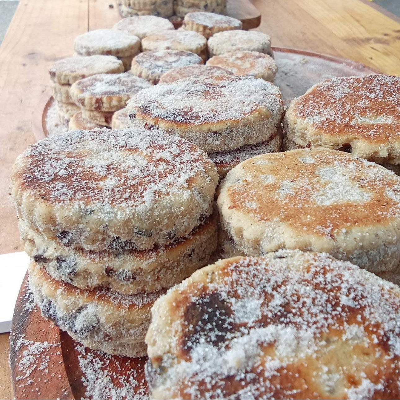 Stacks of Dragonstone Bakes Welsh Cakes sprinkled with caster sugar on a wooden board.