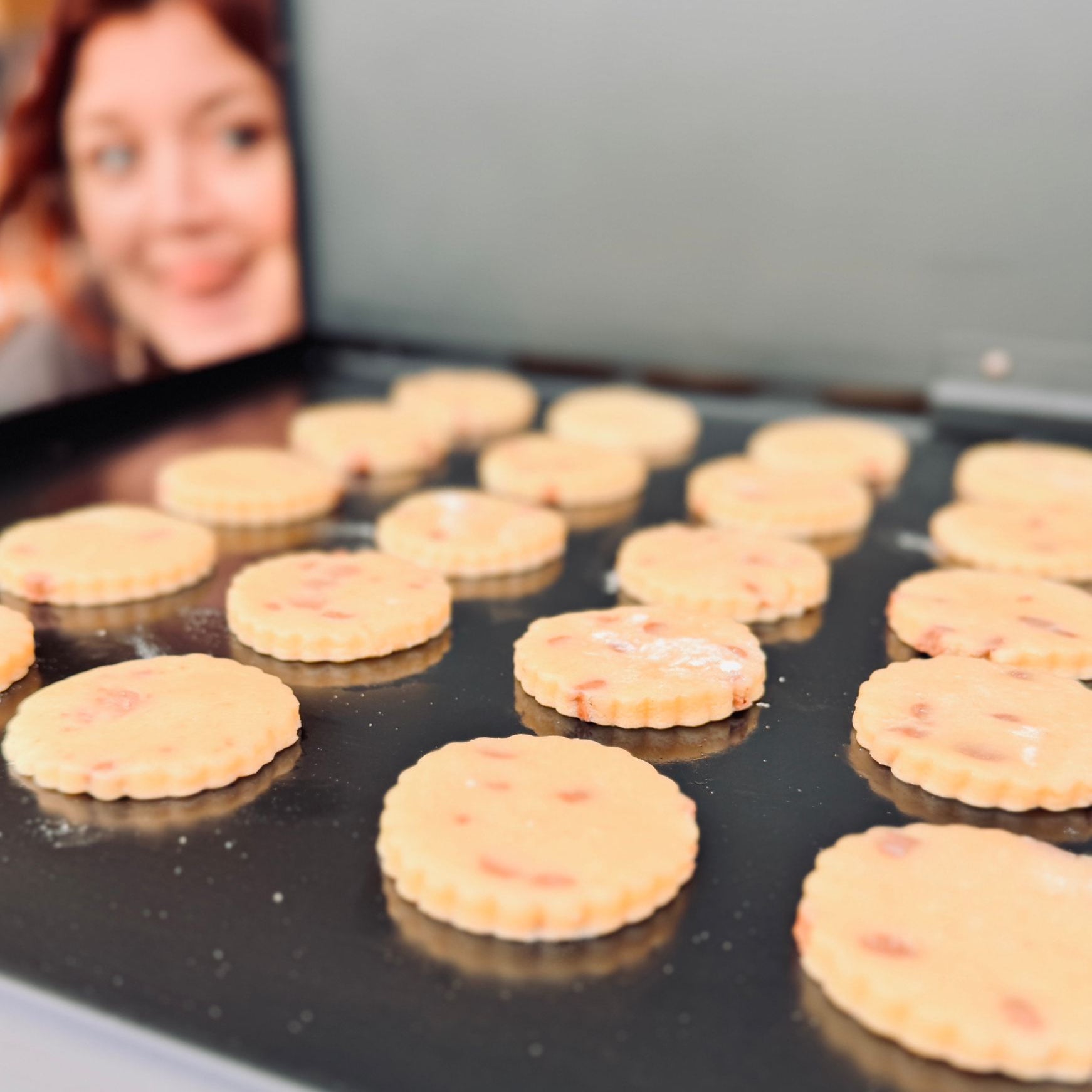 Uncooked Welsh Cakes on a baking tray with a blurred person poking out their tongue in the background. Dragonstone Bakes.