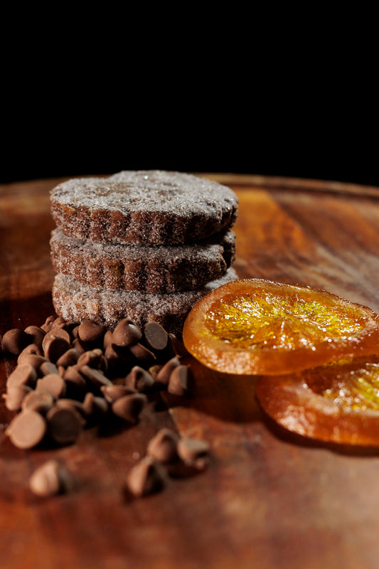 Chocolate Orange Welsh cakes on a wooden board surrounded buy milk chocolate pieces and glace orange slices