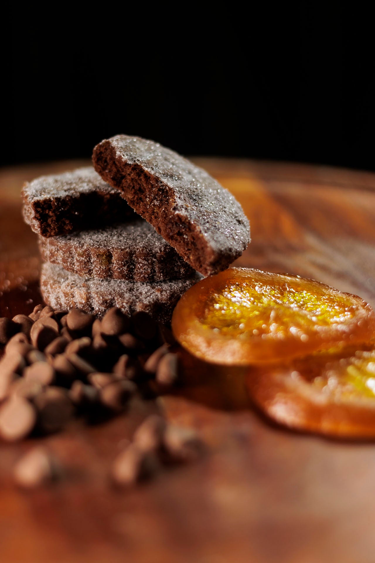 Chocolate Orange Welsh cakes on a wooden board surrounded buy milk chocolate pieces and glace orange slices